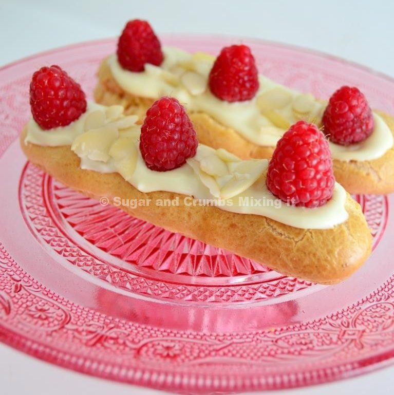 Raspberry Ripple White Chocolate Eclairs topped with fresh raspberries and flaked almonds